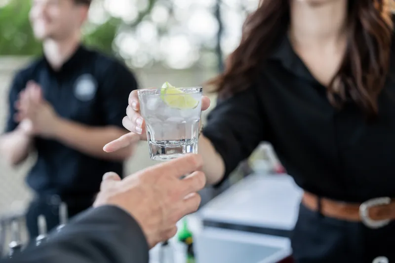 Hands clink together holding glasses of clear cocktail during an outdoor celebration at River House Events, St. Augustine.