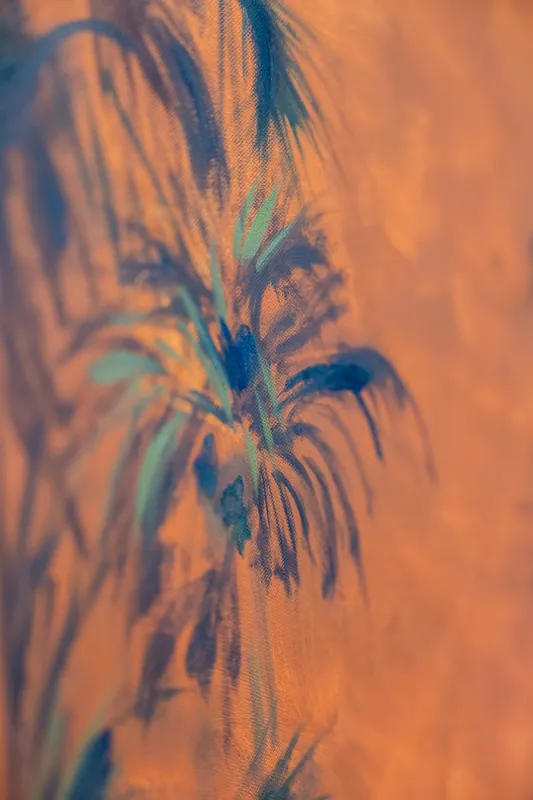 Close-up of blue and green palm fronds painted across the orange canvas surface.