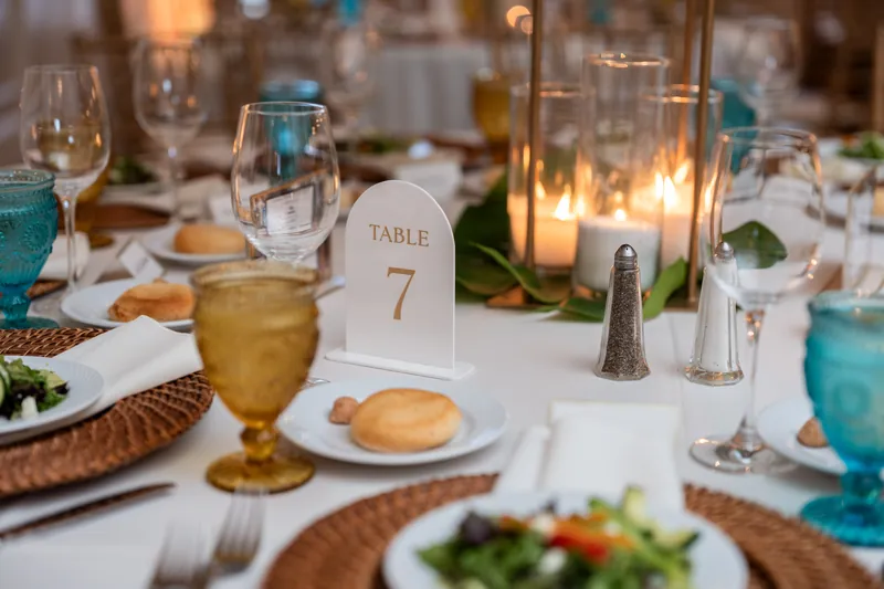 Formal table setting with woven chargers, golden goblets, bread roll, and candlelit centerpiece at River House Events.