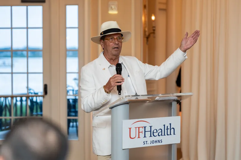 Speaker in a white linen suit and panama hat gestures from a UFHealth podium at River House Events.