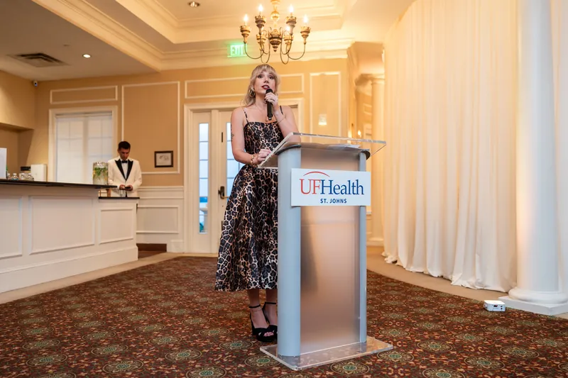 Person in a sequined black dress stands at a UFHealth podium in an elegant cream-and-gold hallway.