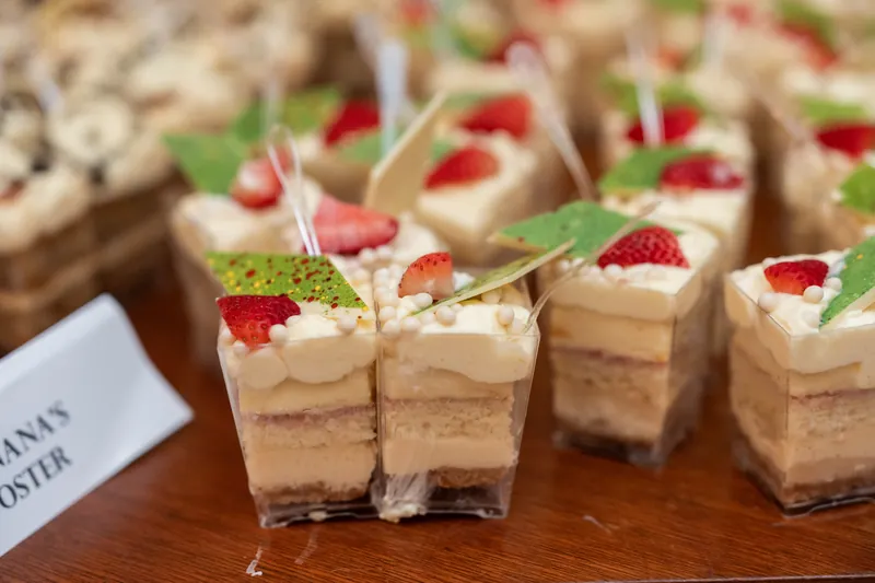 Layered dessert cups topped with whipped cream, fresh raspberries, and mint leaves are arranged in rows on a serving table.