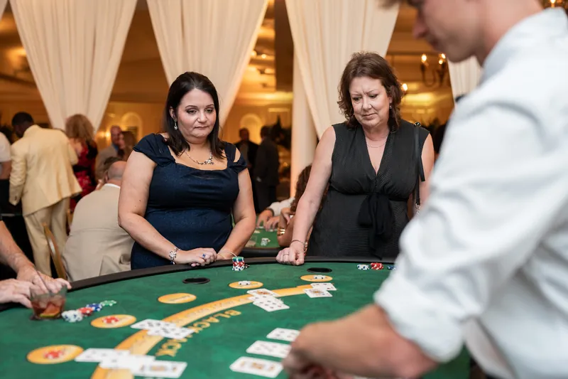 Two women in dark attire place bets on cards laid across the felt surface of a blackjack table at River House Events.