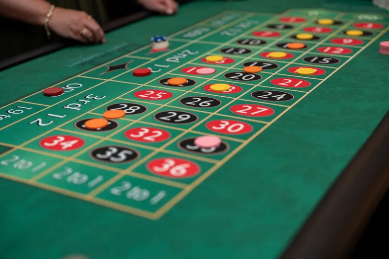 Hands hover over a roulette wheel's betting grid, with chips positioned on various numbered squares during active play.