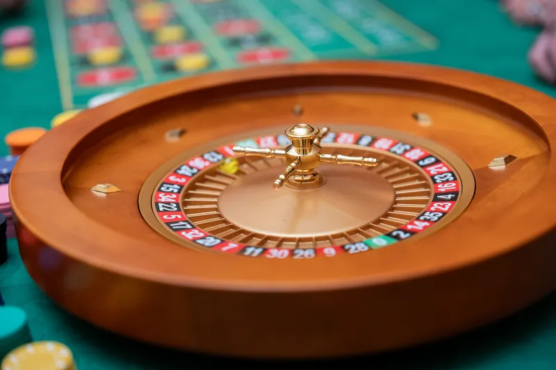 A wooden roulette wheel with numbered compartments and gold trim sits centered on the green felt gaming table.