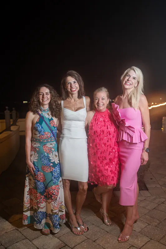 Four women in colorful dresses pose together on River House Events' terrace at night.