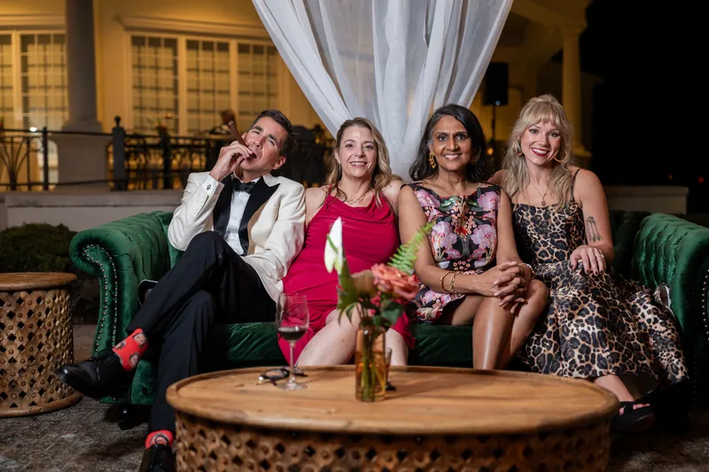 Four guests in formal wear sit on a green sofa with drinks at River House Events.