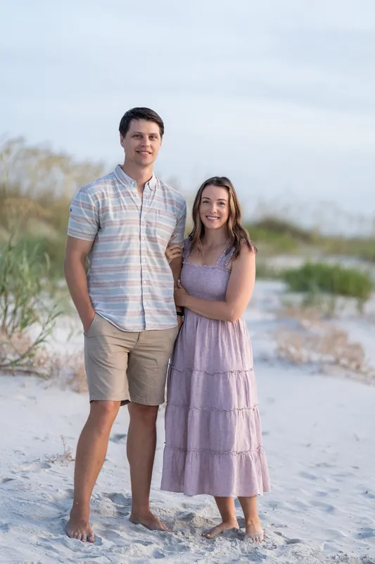 Jourdan and her partner stand together on the beach at St. Augustine, with dunes and sea grass visible behind them