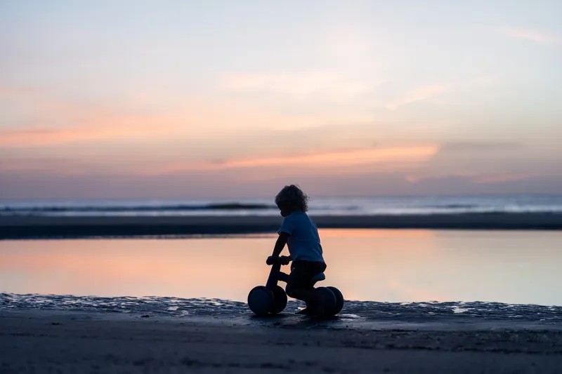 A woman sits alone at the water's edge at St. Augustine Beach during golden hour, silhouetted against the sunset