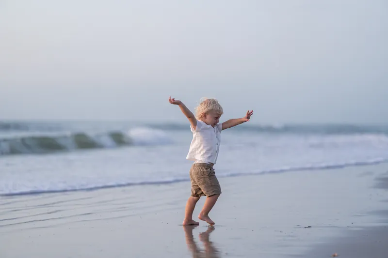 A young child leaps with arms raised on the wet sand at St. Augustine Beach, waves rolling in behind them.