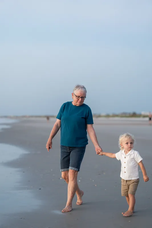 A man and small child walk barefoot across the wet sand at St. Augustine Beach under a clear sky.