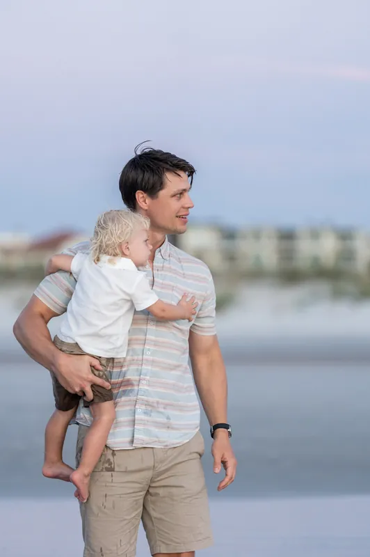 Man holds his young son while gazing toward the water, with the beach stretching behind them at St. Augustine Beach.