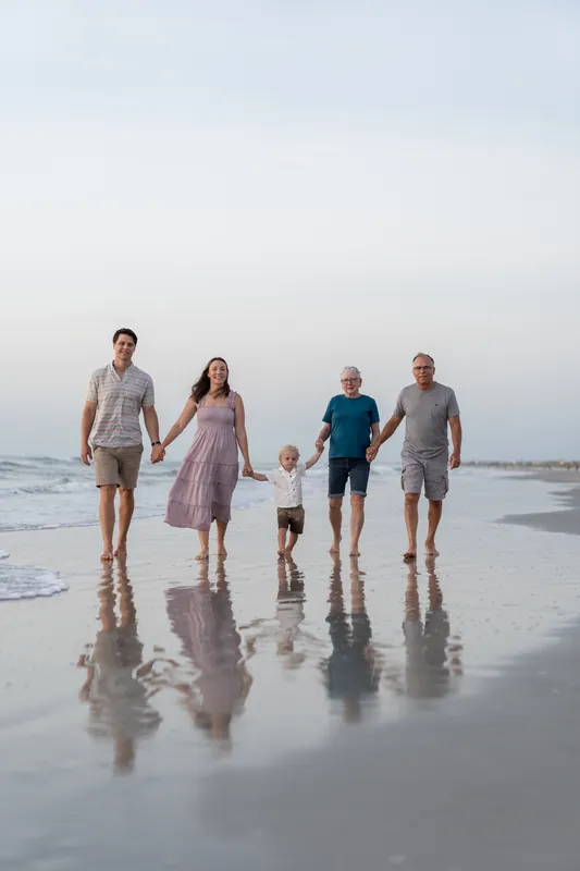 Jourdan's family walks barefoot together along the wet sand at St. Augustine Beach, holding hands under an overcast sky.