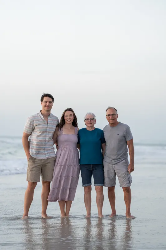 Four adults stand facing the camera in shallow water at St. Augustine Beach, dressed in casual summer clothes.