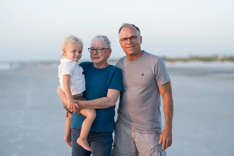 Older man, middle-aged woman, and young boy pose together on the sand at St. Augustine Beach during golden hour light.