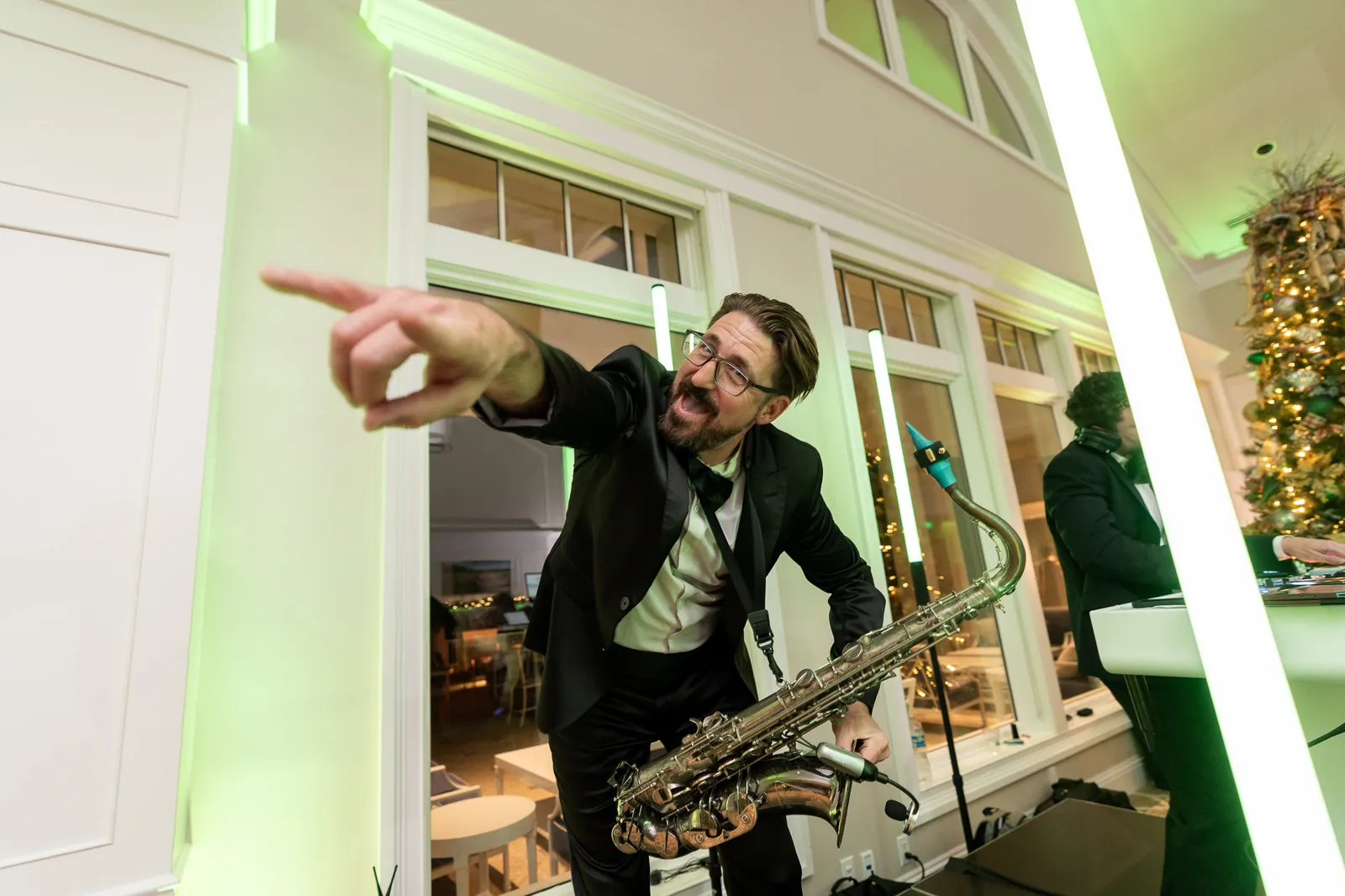 Corey of COS Celebrations playing saxophone under green uplighting at a wedding reception.