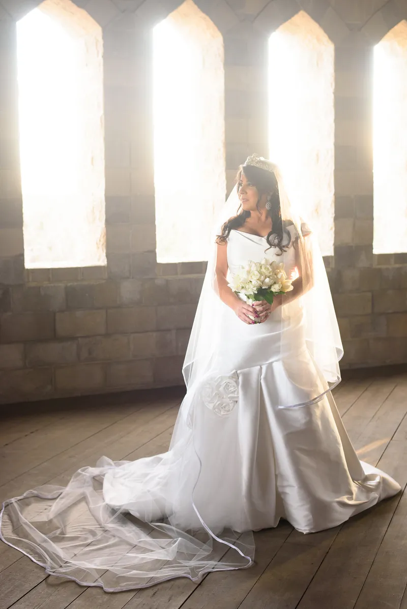 Bride with flowing veil backlit by gothic windows inside Castle Ottis St. Augustine