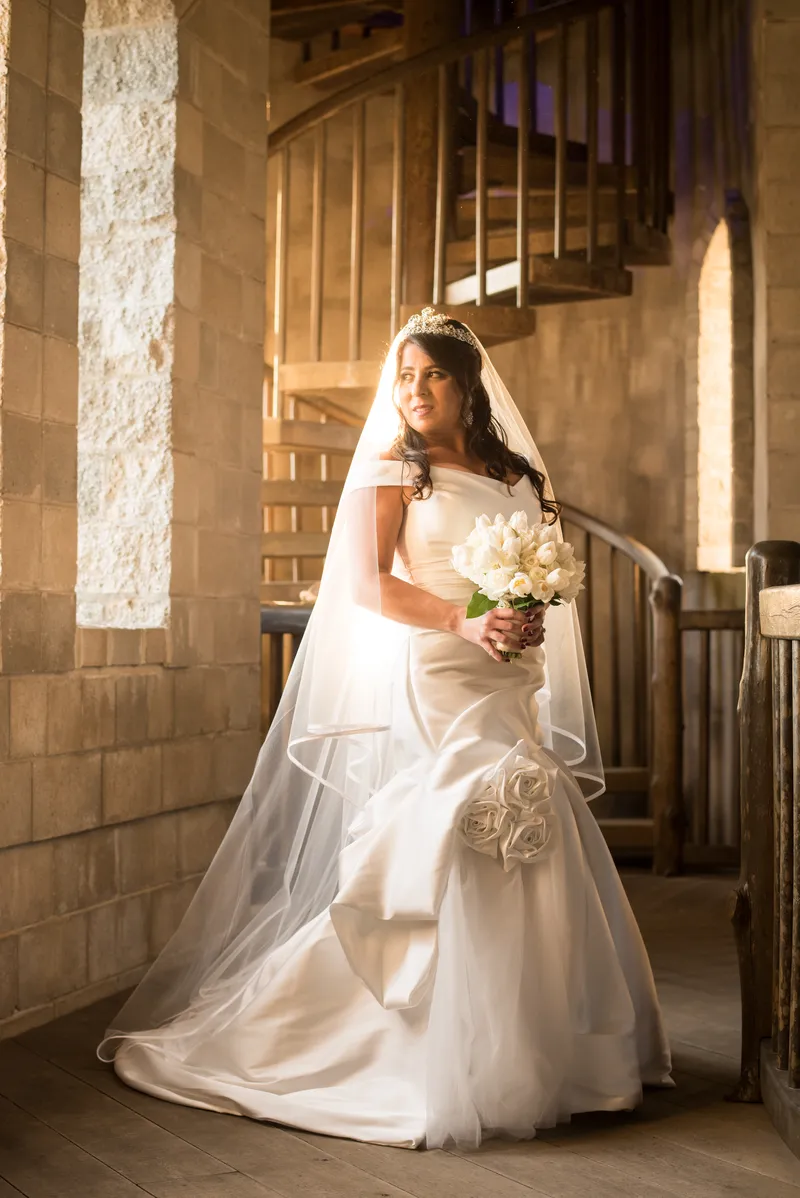 Full-length bridal portrait by spiral staircase in golden light at Castle Ottis