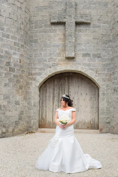 Full-length bridal portrait at Castle Ottis wooden doors with stone cross and coquina walls
