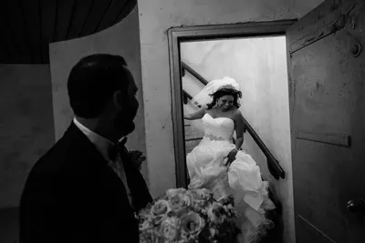 Black and white photo of bride descending spiral staircase through doorway with groom waiting at Castle Ottis