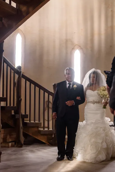 Father walking bride down the aisle with light streaming through gothic windows at Castle Ottis wedding