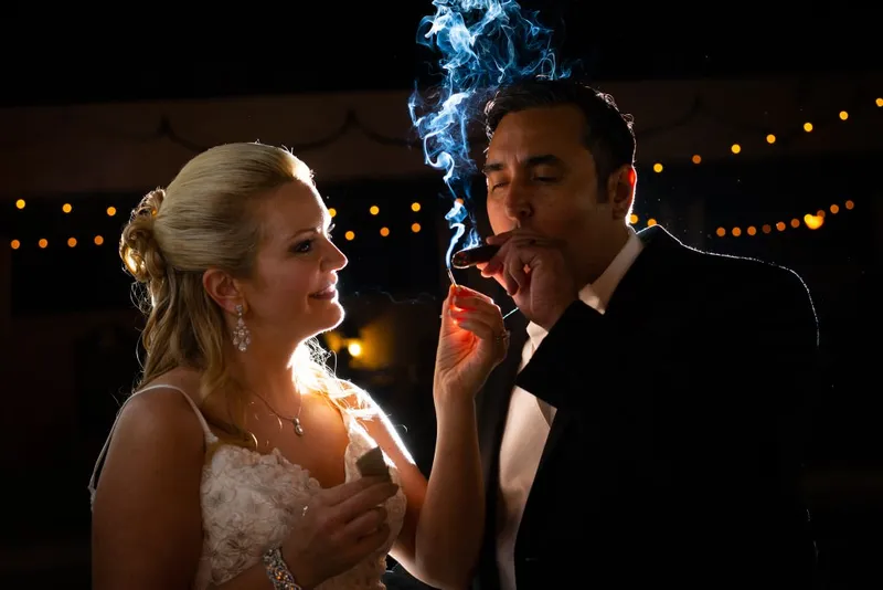 Bride lights husband cigar at wedding reception