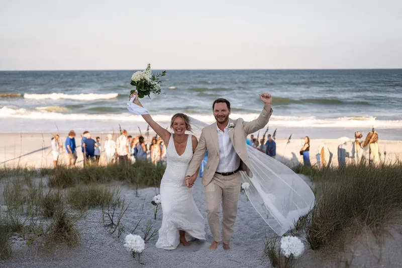 Couple celebrating walking up sand dunes after beach ceremony
