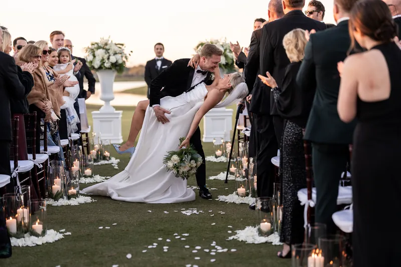 Groom dipping bride for kiss at golf course ceremony with candles