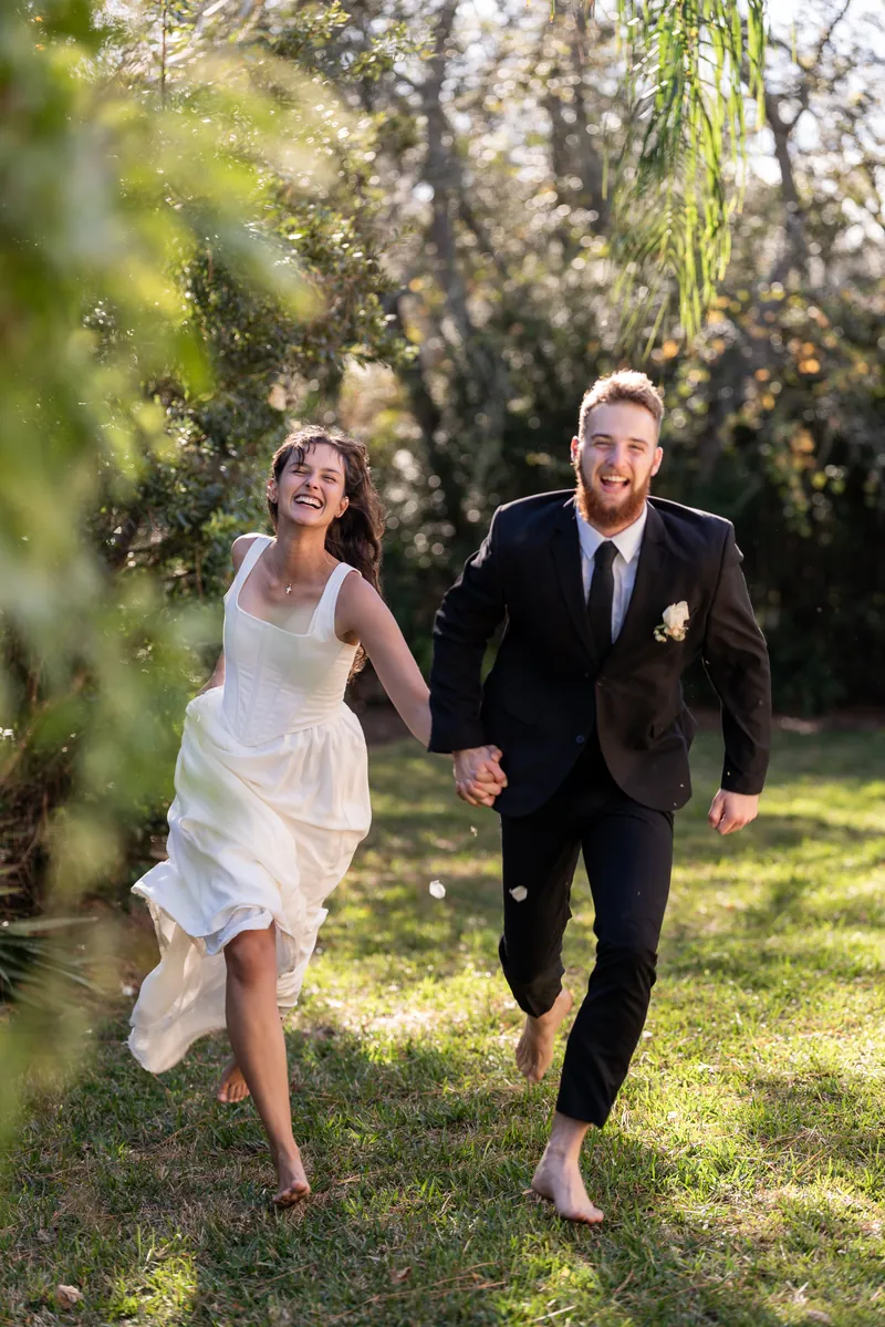 Couple running and laughing through garden on wedding day