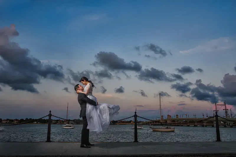 Groom lifting bride at bayfront with Bridge of Lions at sunset