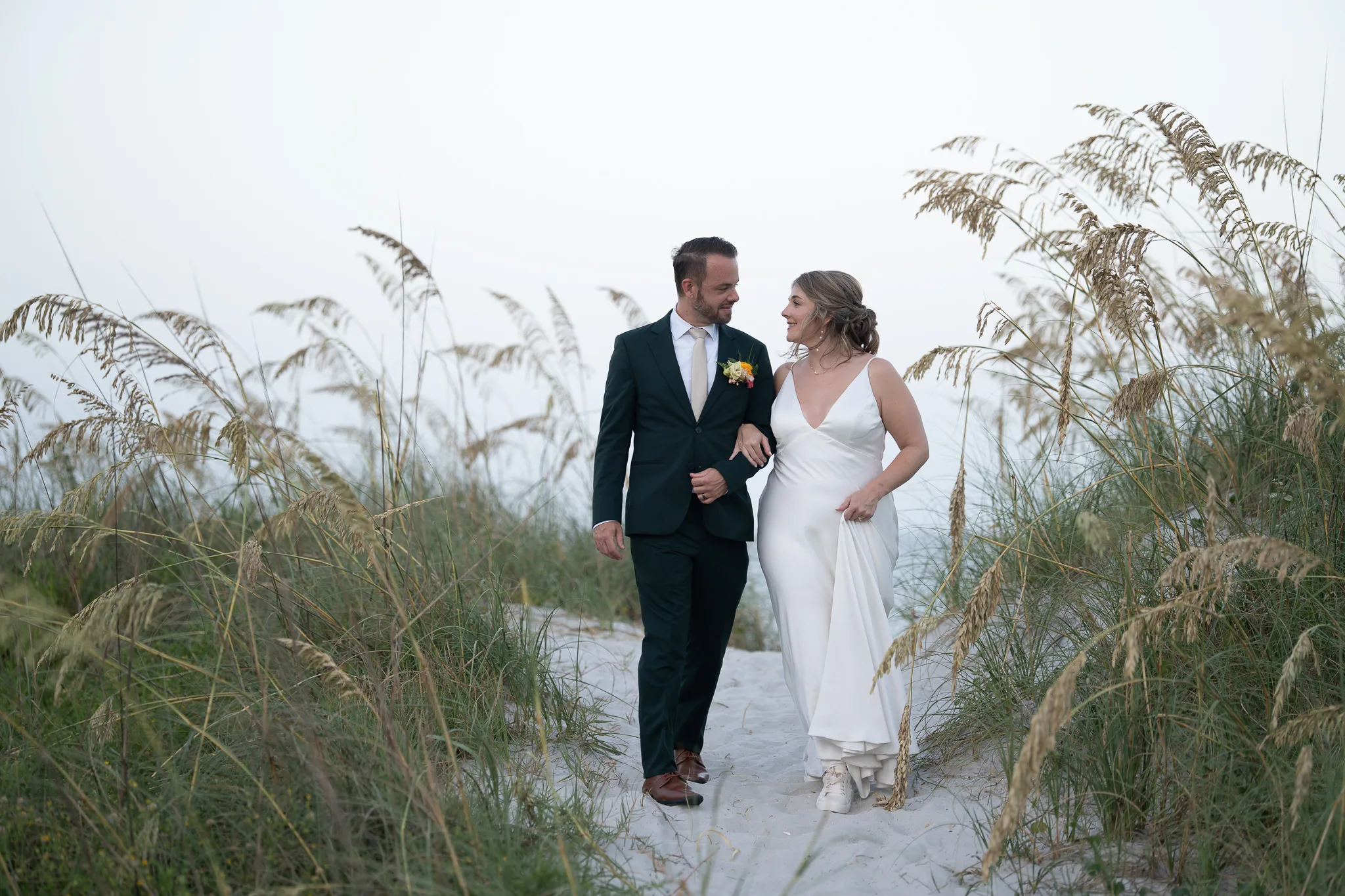 bride and groom embrace with sea oats on the dunes at the beach