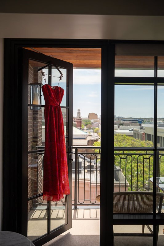 0005_A vibrant red dress hanging in an open doorway with a cityscape view in the background.jpg