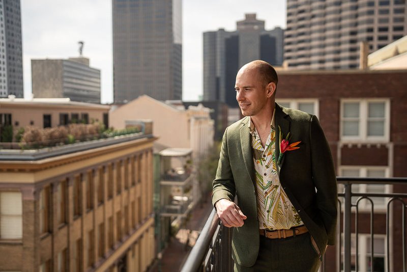 0010_A man in a green suit and floral shirt stands on a city balcony looking out thoughtfully.jpg