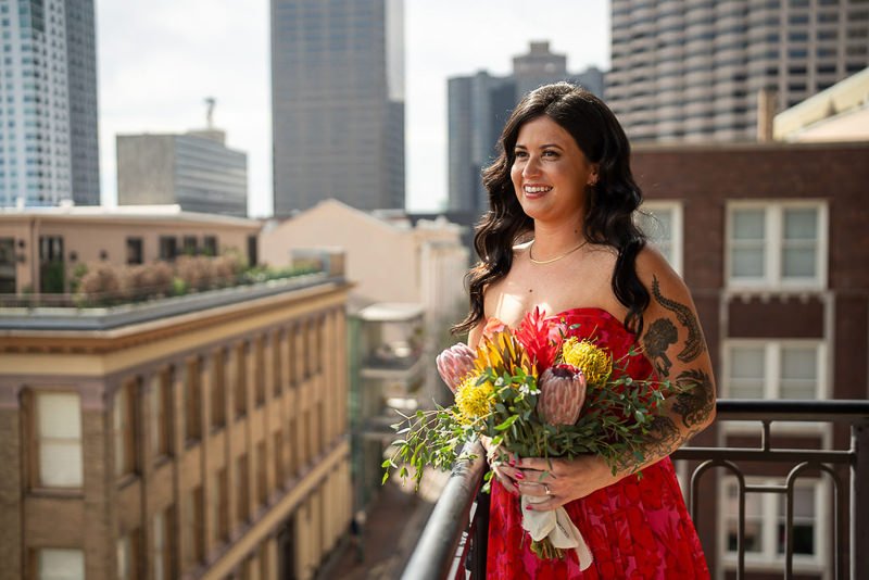 0011_Woman in a red dress holding a bouquet on a balcony overlooking a cityscape.jpg