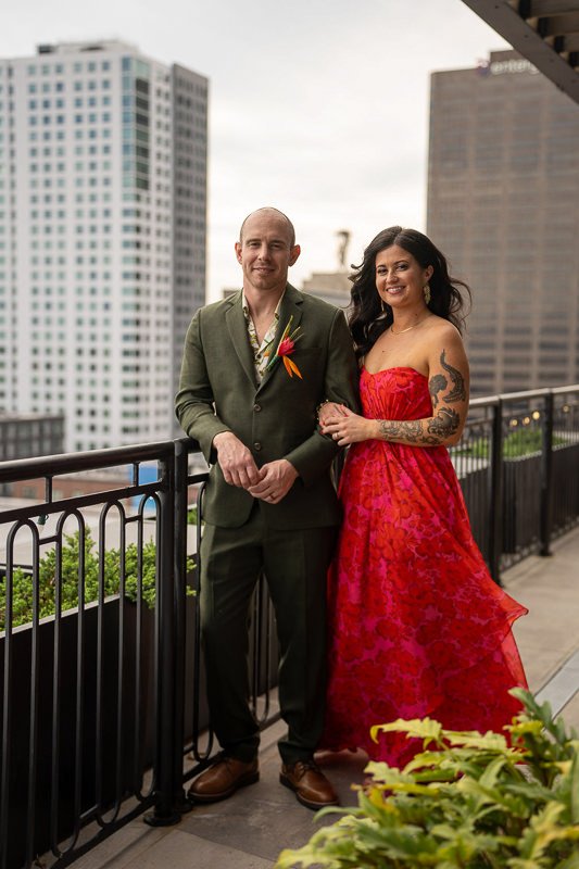 0017_Couple posing on a city balcony he in a green suit she in a red dress with tall buildings in the background.jpg