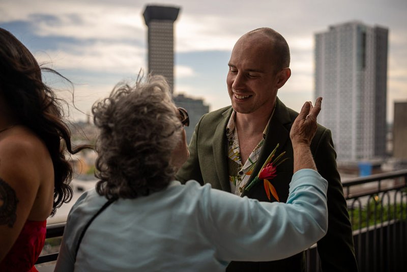 0020_A smiling man in a suit shares a heartfelt moment with an elderly woman on a balcony.jpg
