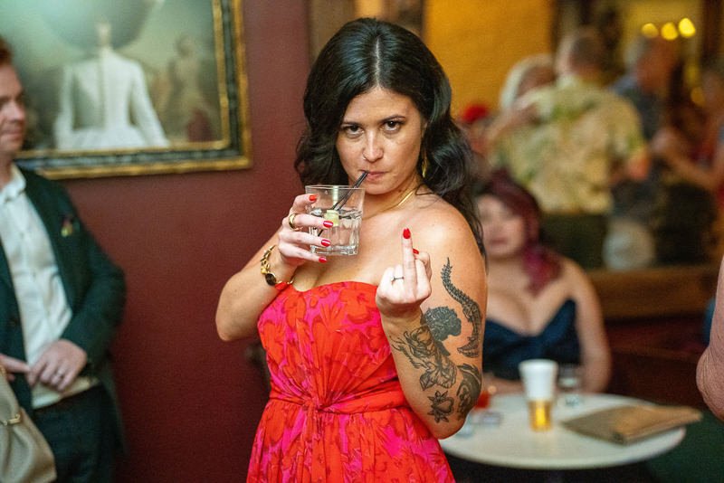0038_Woman in a red dress making a bold gesture while holding a drink at a lively gathering.jpg