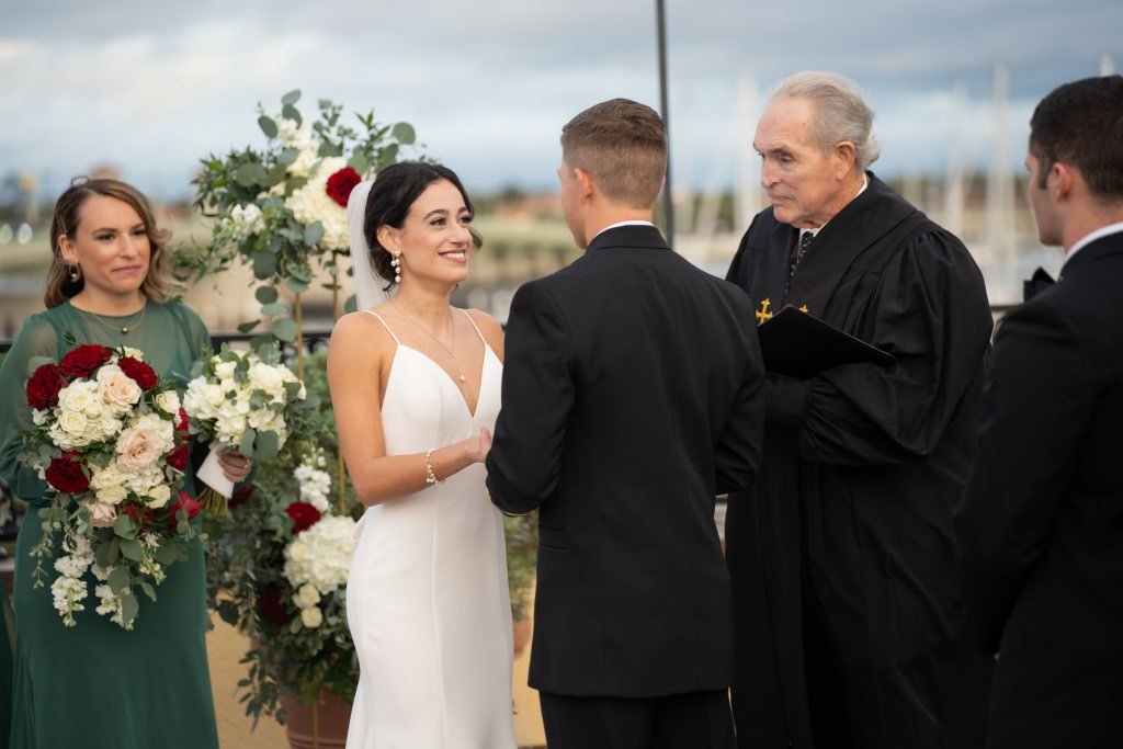 A bride and groom exchange vows at their outdoor wedding ceremony surrounded by attendants and adorned with floral arrangements.jpg