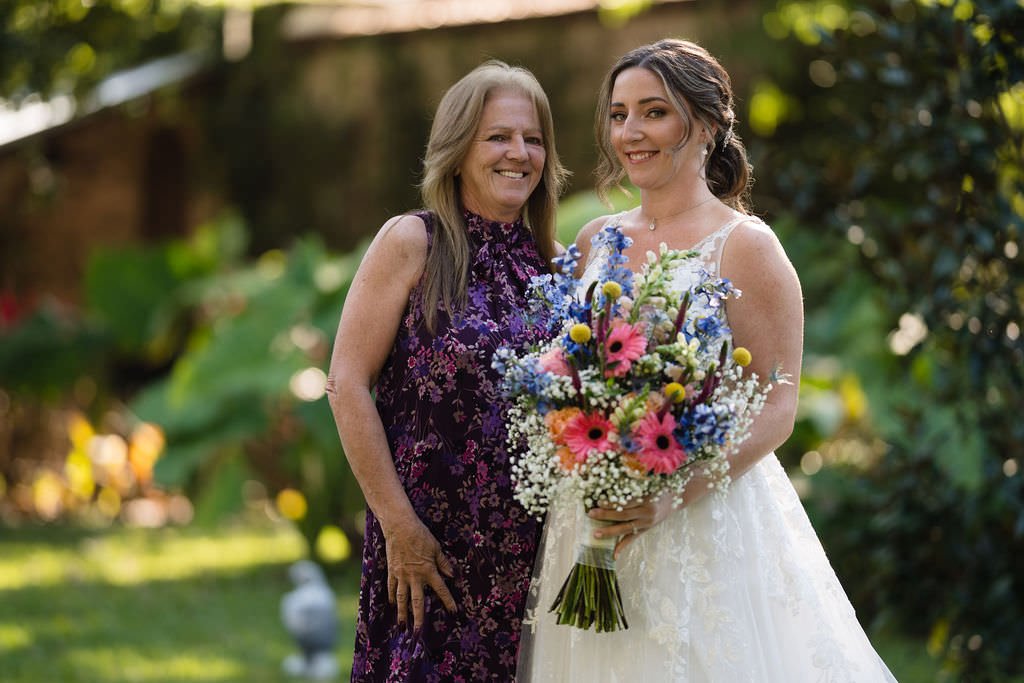 A bride beams with joy alongside her mother holding a vibrant bouquet weddingday motherofthebride love.jpg