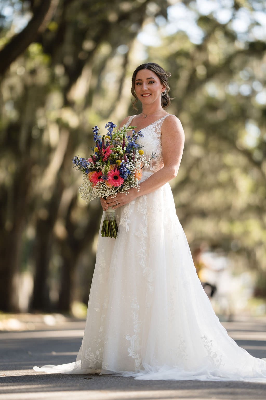 A bride stands in the middle of a tree lined street her smile as bright as her bouquet.jpg