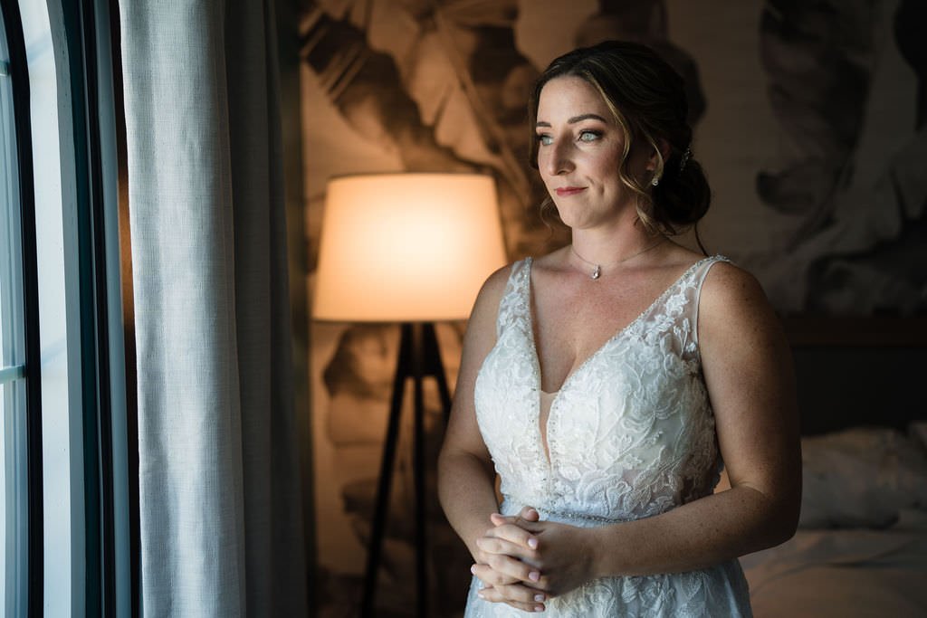 A bride to be looks out the window contemplating the day ahead She is radiant in her beautiful wedding dress.jpg