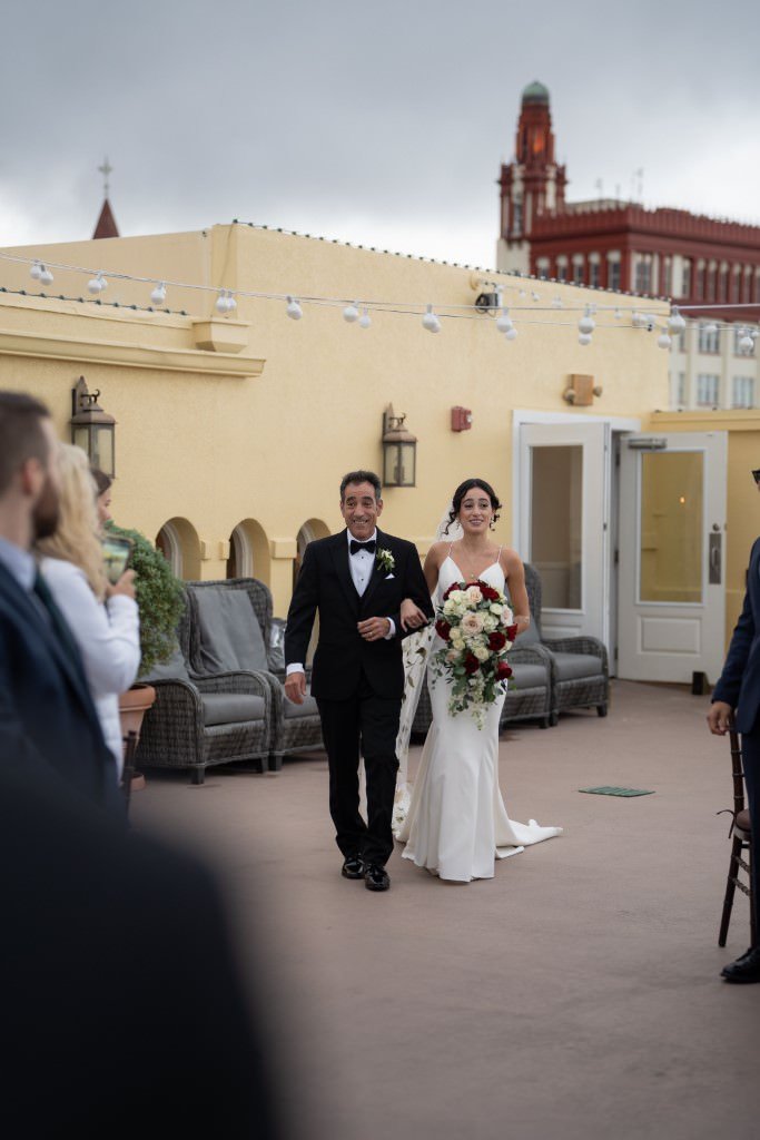 A bride walks down the aisle with her father on a rooftop surrounded by guests.jpg