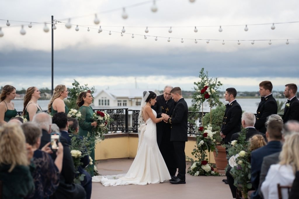 A couple exchanges vows during an outdoor wedding ceremony under string lights with the ocean in the background.jpg