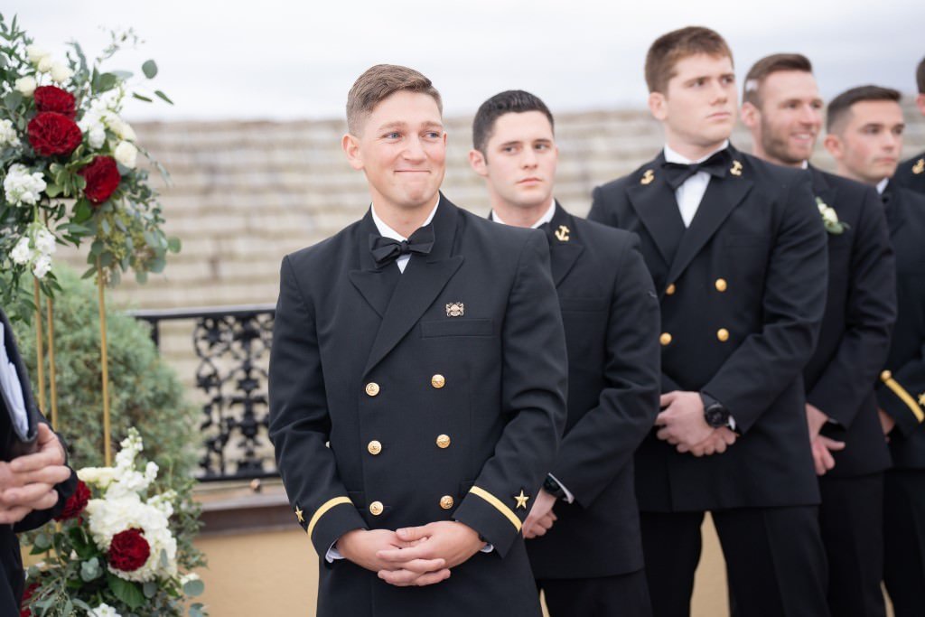 A group of men in formal military uniforms stand in an outdoor ceremony with one at the front smiling.jpg