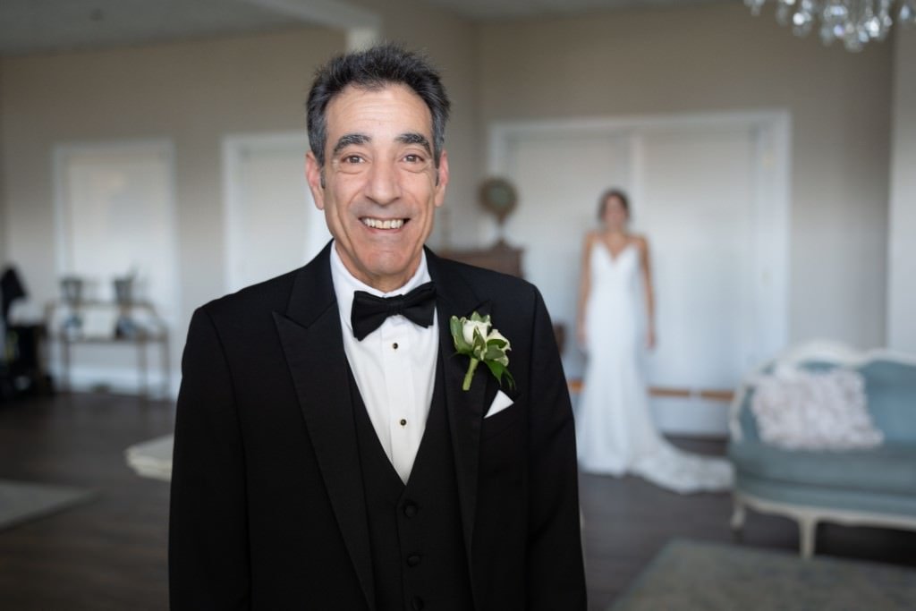 A joyful man in a tuxedo with a woman in a bridal gown in the background.jpg