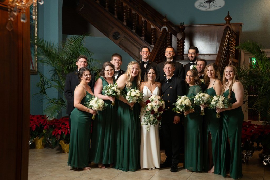 A joyful wedding party with bridesmaids in green dresses and groomsmen in black suits posing on a staircase.jpg