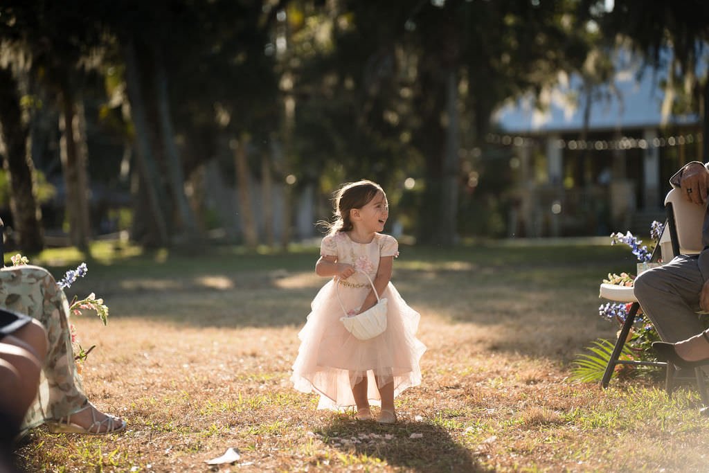 A little flower girl in a pink dress walks down the aisle at an outdoor wedding.jpg