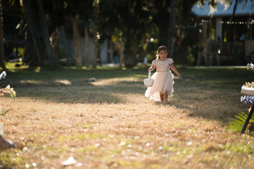 A little girl in a flower girl dress walks down the aisle ready to spread the.jpg