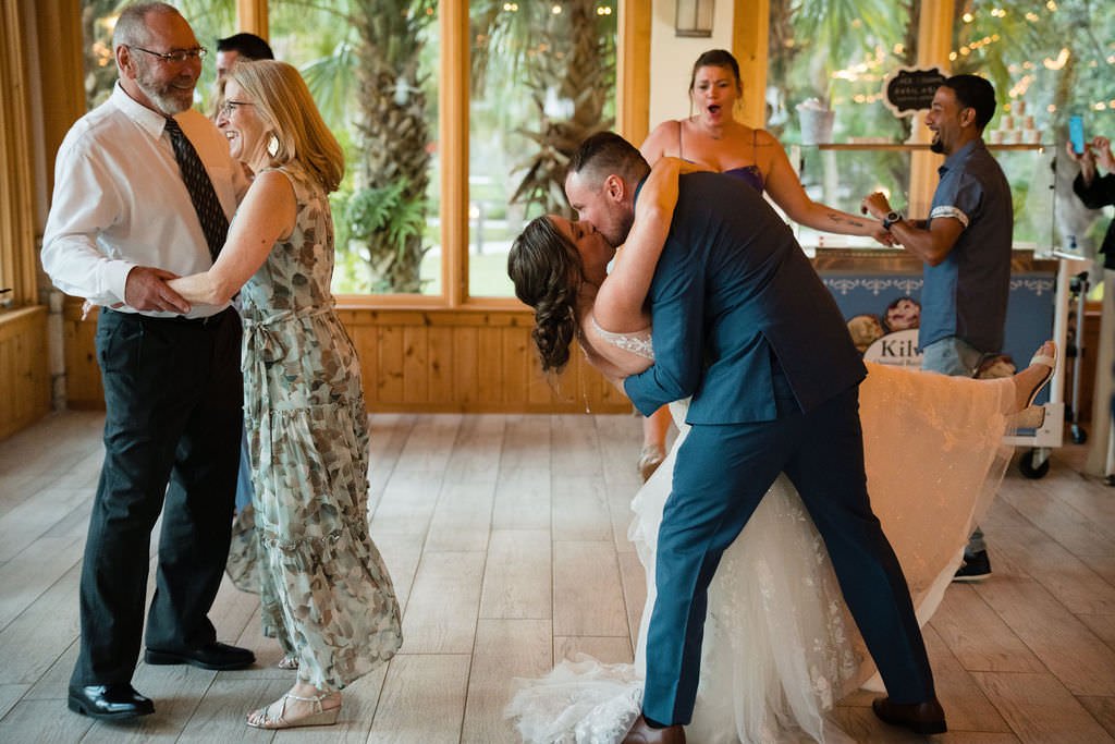 A newly married couple shares a kiss on the dance floor surrounded by family and friends at their wedding reception.jpg