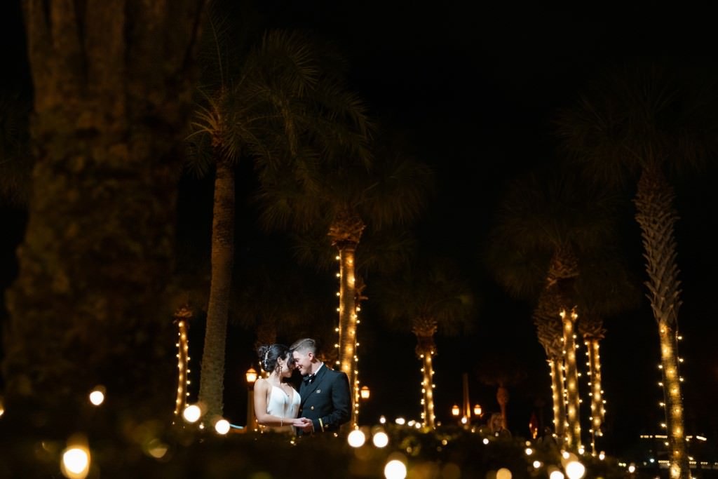 A newlywed couple shares a tender moment under twinkling lights and palm trees at night.jpg
